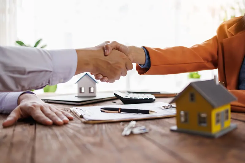 Aperto de mãos sobre contrato com miniatura de casa, segurança e transparência